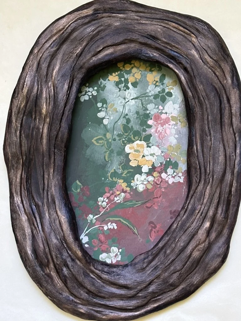 An oval hand-built ceramic frame holding a painting of blossom on a dark ground